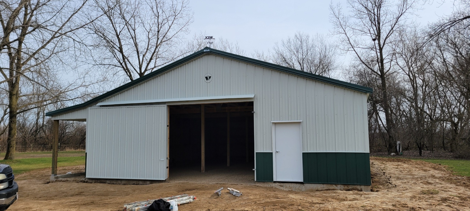 White post-frame building with green wainscot and open large end-wall door