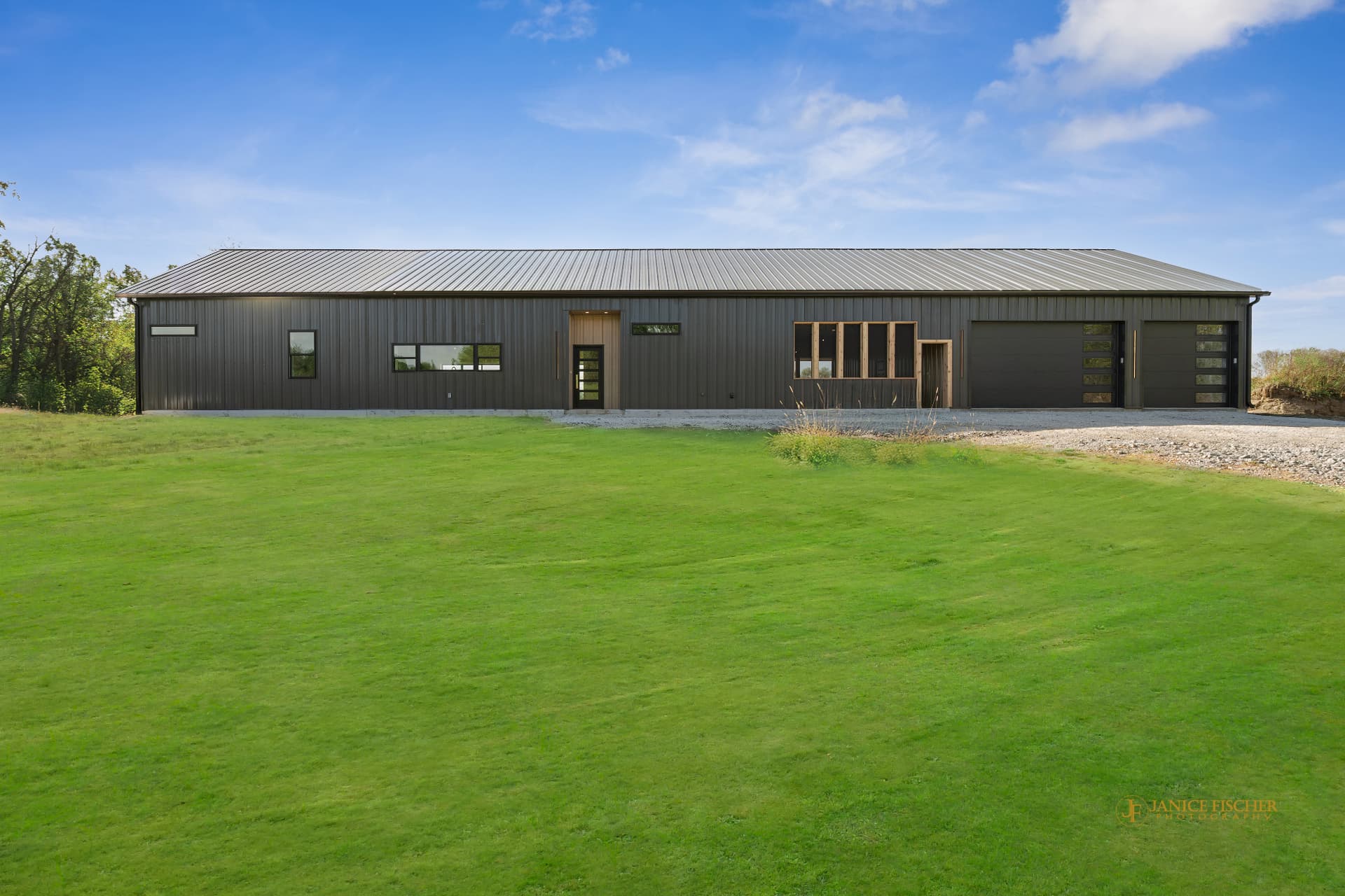 Custom Bella model barndominium with dark metal siding and multiple overhead doors viewed across a green lawn