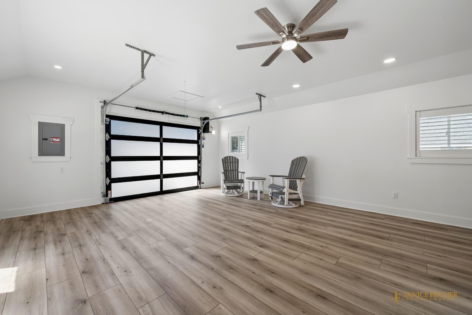 Finished garage interior with glass panel overhead door, ceiling fan, and wood-look flooring