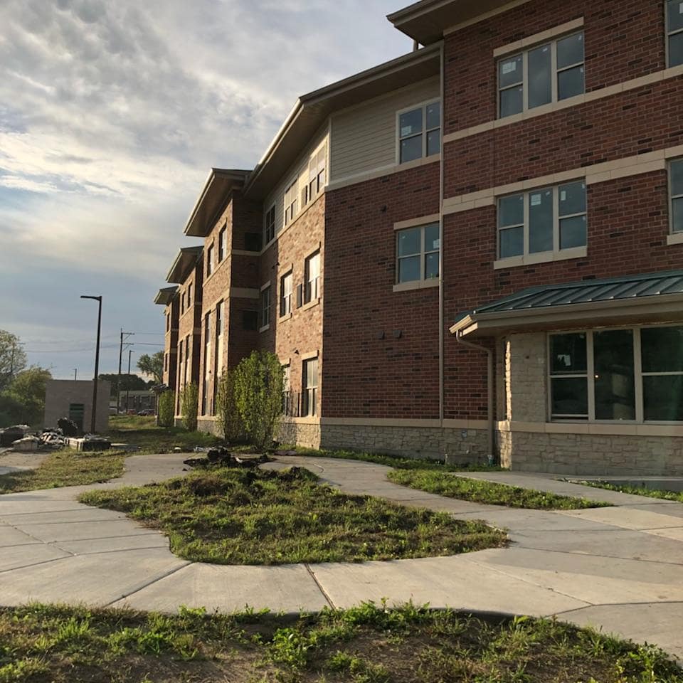 Three-story brick and stone senior living community exterior with landscaped walkways and young plantings
