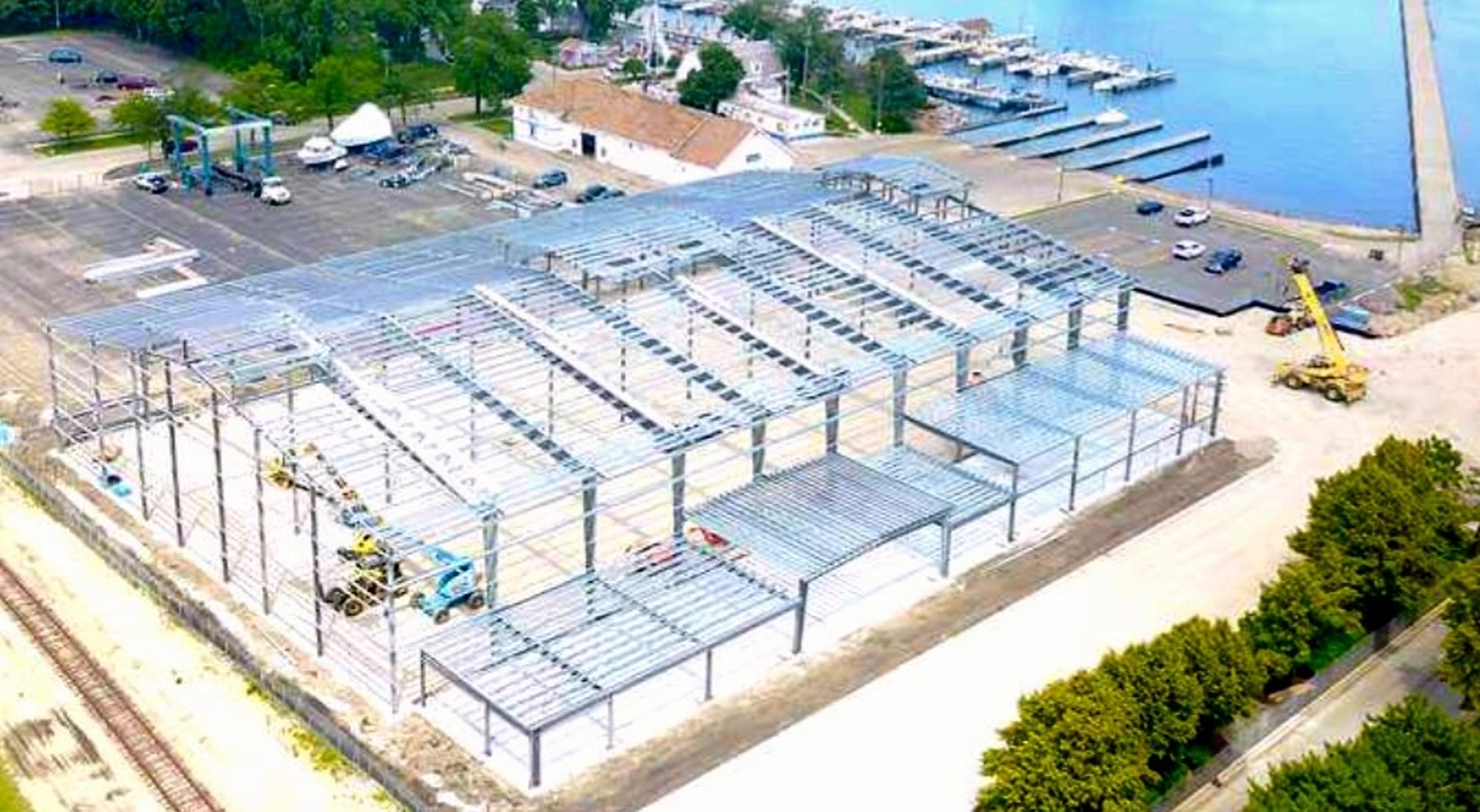 Aerial view of a large steel building frame under construction beside a marina