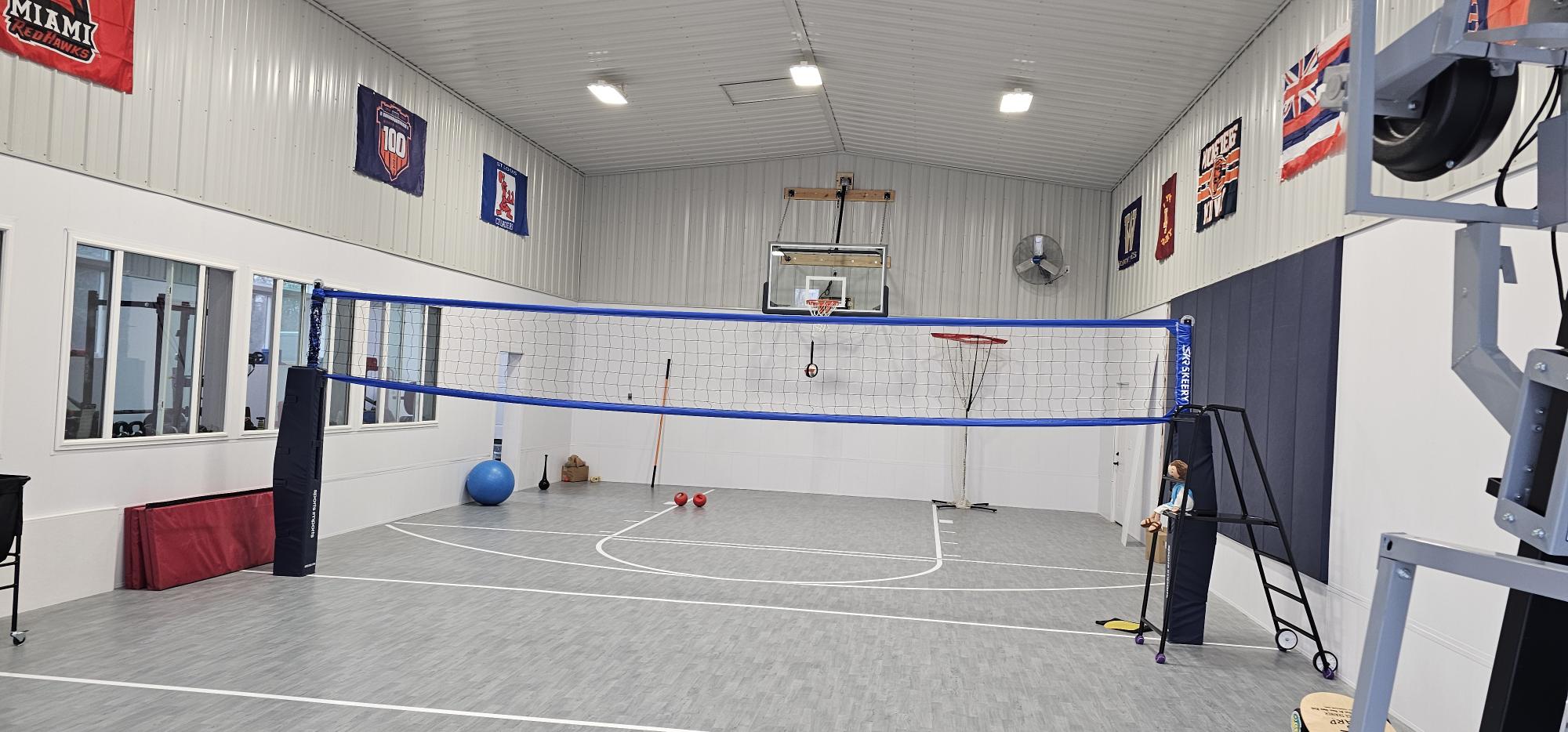 Indoor volleyball court with net, basketball hoop, sport tile flooring, and padded walls inside an agricultural building