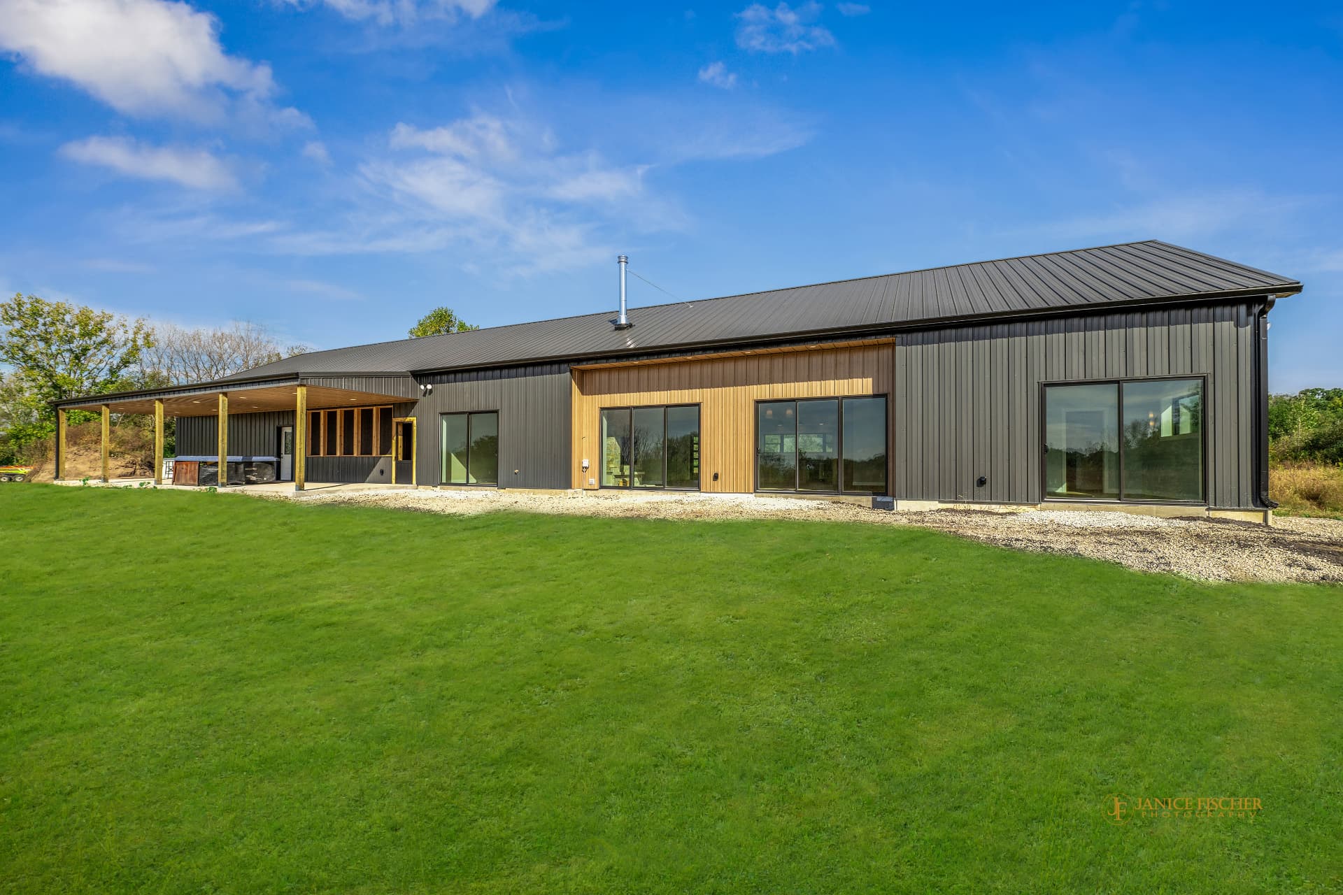 Completed custom barndominium exterior with dark metal siding, wood-accent porch, and sliding glass doors